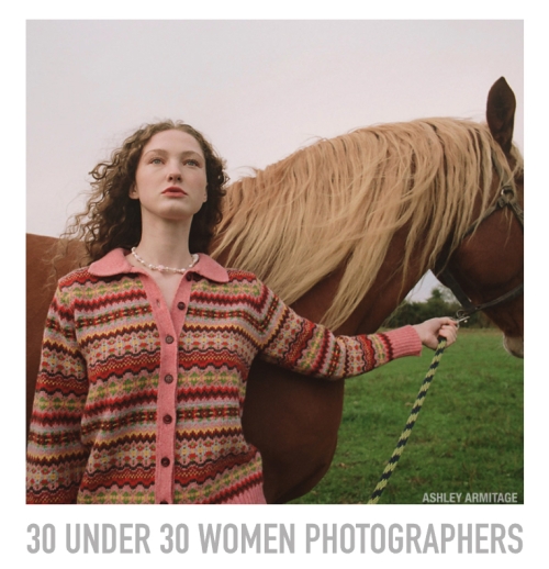Woman in patterned sweater holds lead rope of a light brown horse in a grassy field under an overcast sky.