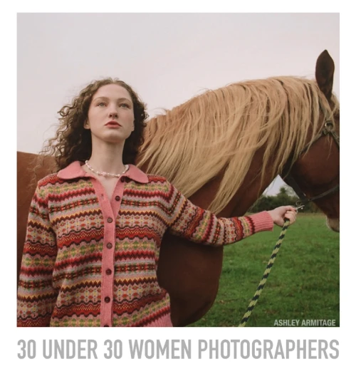Woman in patterned sweater holds lead rope of a light brown horse in a grassy field under an overcast sky.
