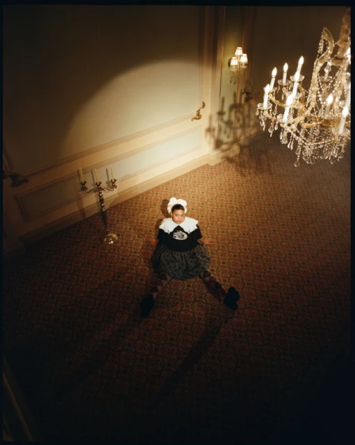 Overhead shot of a woman in a decorative dress sitting on a patterned floor in an elegant foyer with a chandelier.