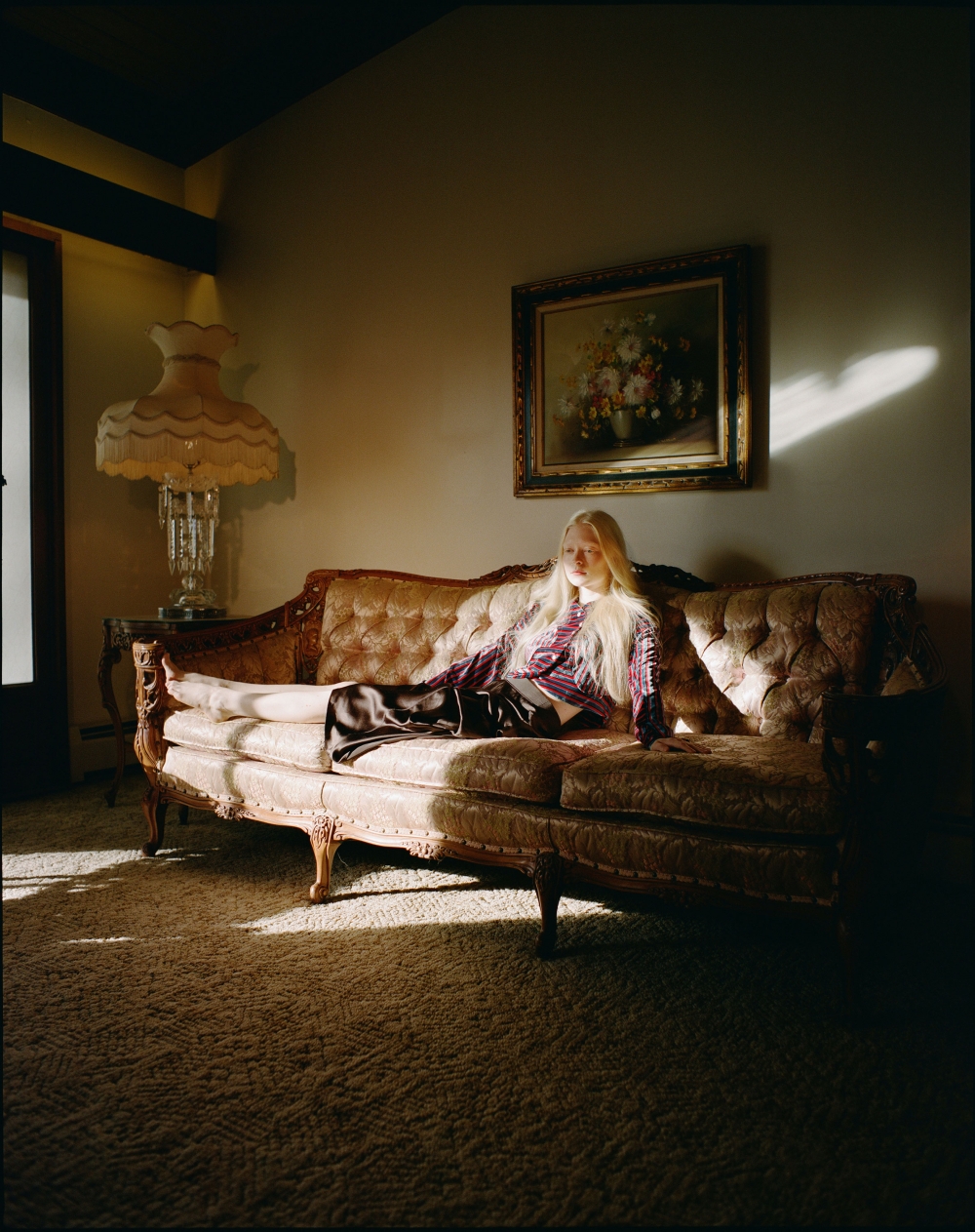 Blonde woman reclining on a patterned tufted sofa in a dimly lit living room captured by Ashley Armitage