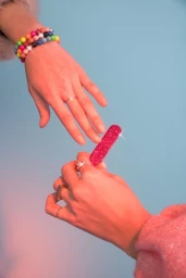 Two hands reaching towards each other, one wearing colourful beaded bracelets and a ring, against a blue background.