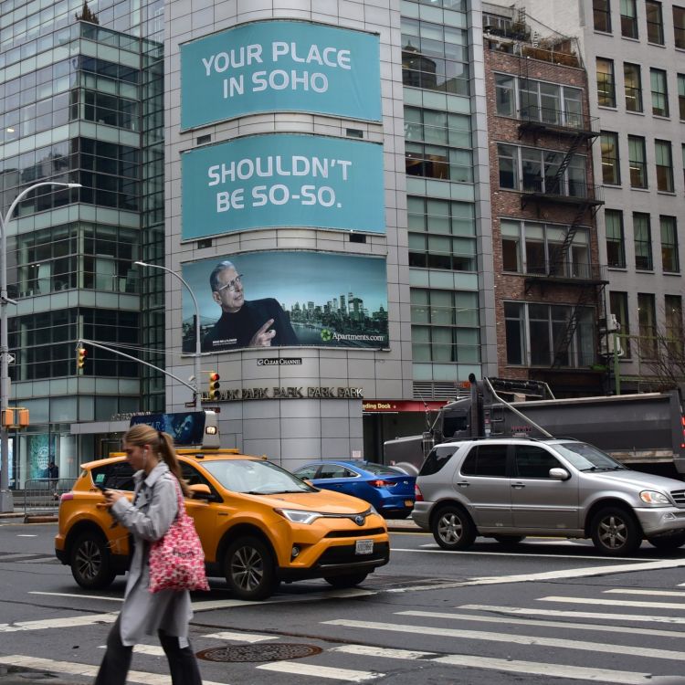 Street scene in SoHo, New York, featuring a pedestrian crossing, yellow taxi, and buildings with billboards and architectural details.