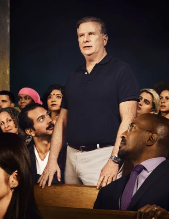 Image of a man standing, addressing a diverse crowd seated in rows, wearing business attire and semi-formal wear in an indoor setting.