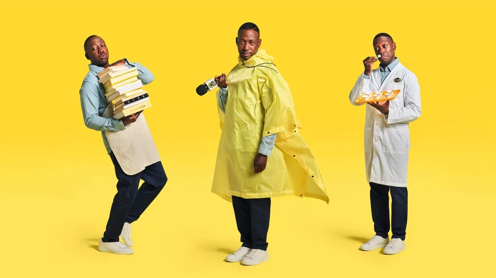 Three Black adult males pose in a bright yellow studio backdrop. One holds books, another a microphone, and the third samples food.