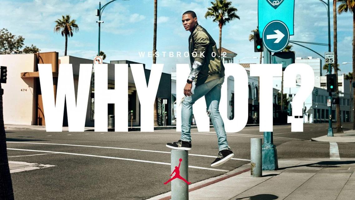Athlete in olive jacket and jeans stands on bollard in urban setting with palm trees and buildings under a clear sky, promoting Westbrook 0.2.