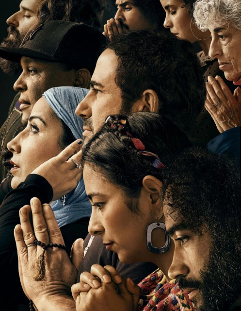Diverse group of people with hands clasped in prayer, heads bowed, and eyes closed, set against a dark background in a close-up portrait.