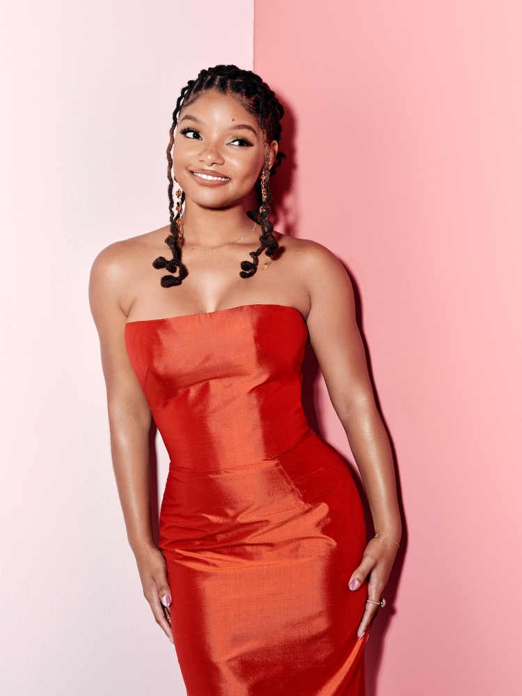 Headshot of a smiling, stylish woman with braided hair wearing a strapless red dress against a two-tone pink background. Beauty shot.