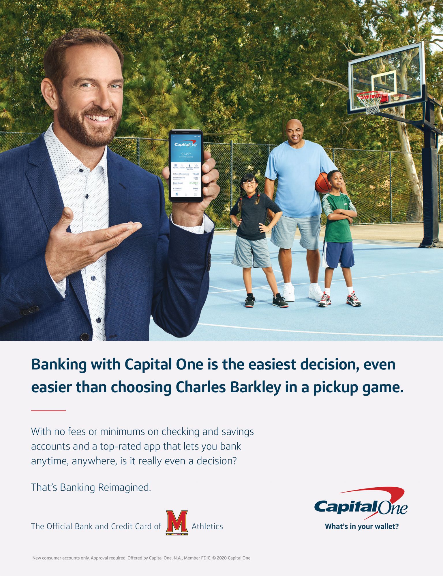 Smiling man in suit points to banking app on his phone with two kids and an adult near outdoor basketball court, Capital One ad.