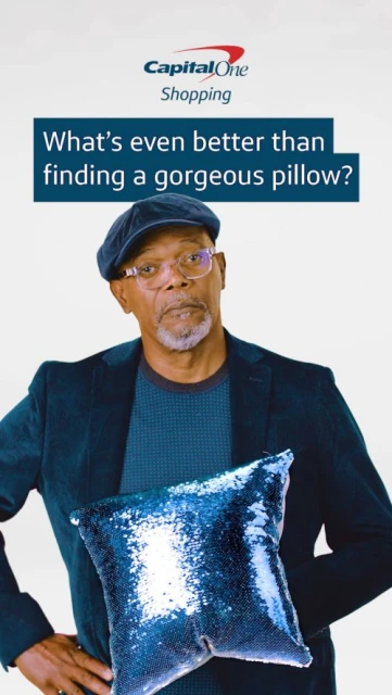 Adult male wearing a blue jacket and hat holding a glittery blue pillow, posing against a white backdrop; Capital One shopping advertisement.