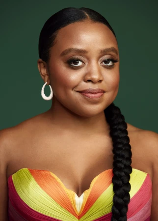 Portrait of a smiling African-American woman with braided hair, wearing a colorful strapless dress against a green backdrop.