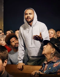 Group of diverse people gathered with a man in a grey hoodie speaking and gesturing outward in a crowd.