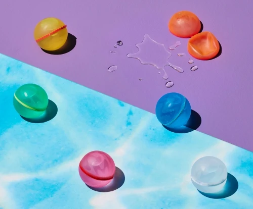 Colorful water balloon toys on a purple and blue background with soft lighting, casting shadows and creating a playful summer scene.