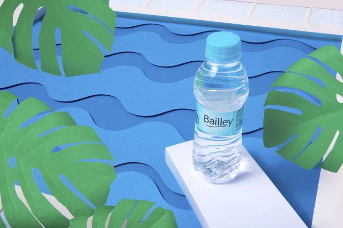 Water bottle on a white platform with a blue paper wave background and green monstera leaf paper cutouts in a studio setting.