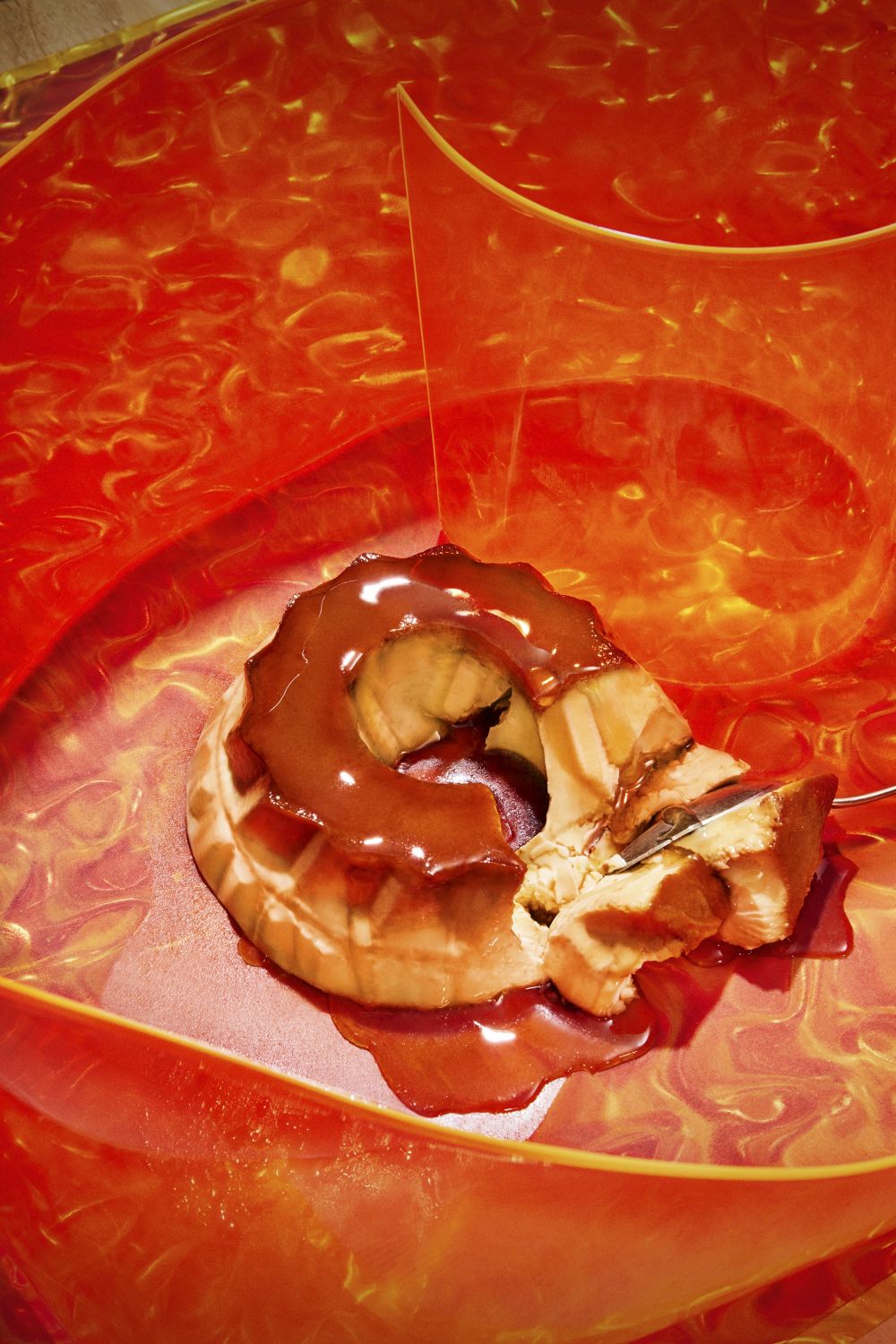 Close-up studio shot of a slice of caramel flan on a vibrant orange plate, highlighting its creamy texture and rich caramel sauce.