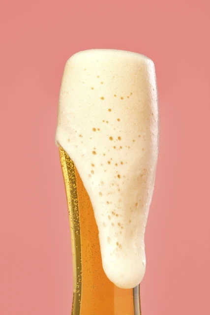 Tall glass of frothy beer with overflowing white foam against a solid light red background, studio shot, beverage photography.