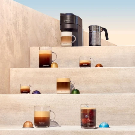 Nespresso coffee machines, clear coffee cups with drinks, and colorful coffee pods are arranged on a clean, neutral staircase.