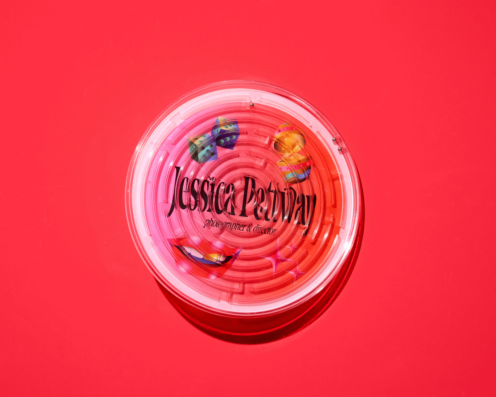 Overhead studio shot of a pink and white plastic maze toy with dice and lip graphics, set against a vibrant pink background.