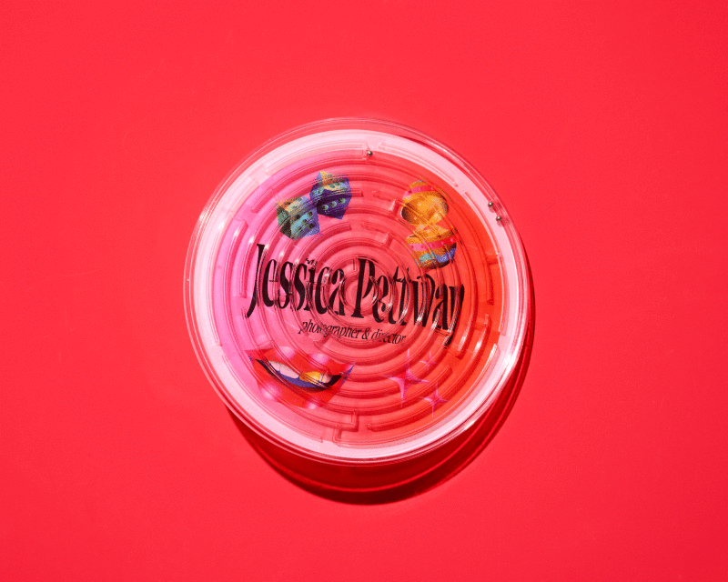 Overhead studio shot of a pink and white plastic maze toy with dice and lip graphics, set against a vibrant pink background.