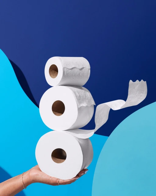 Stack of white toilet paper rolls held in a hand against a blue background with light blue graphic elements.