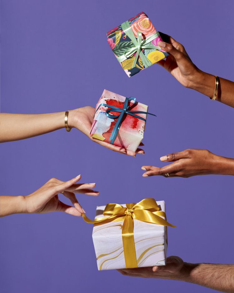 Hands exchange three wrapped gifts with bright ribbons against a vibrant purple background in a celebratory, giving gesture.