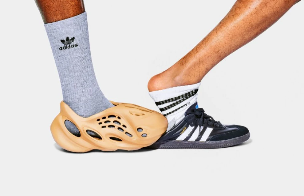 Two feet wearing different Adidas sneakers and socks are juxtaposed against a white backdrop in a studio shot.
