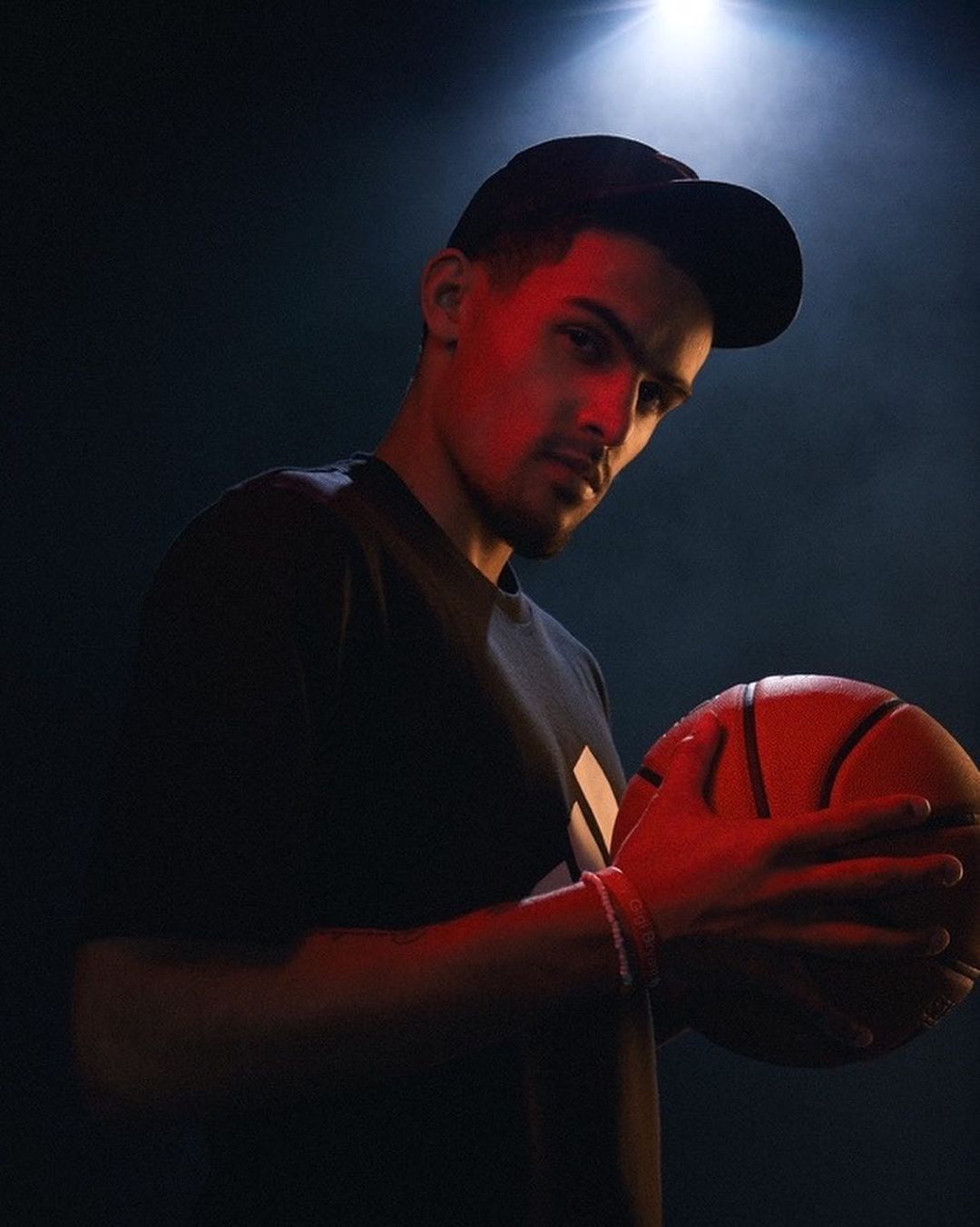 Male athlete holds a basketball while posing in a studio. Head and shoulders shot with dark background and red lighting.