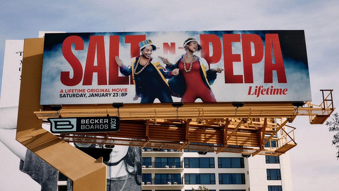 Billboard promoting 'Salt-N-Pepa' Lifetime movie featuring the artists in vibrant outfits, set against a cloudy sky background.