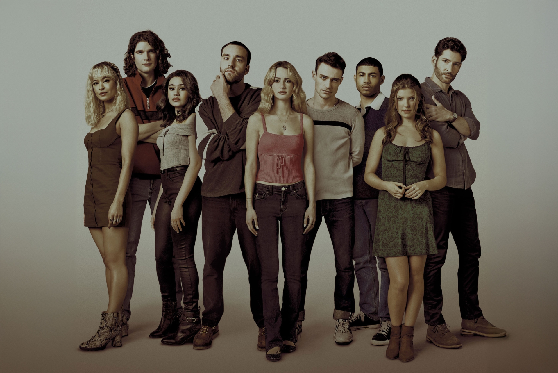 Group of nine people standing indoors in casual clothing, medium shot, neutral backdrop, direct studio lighting, fashion, and entertainment.