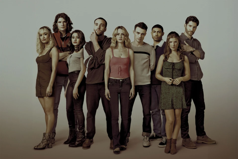Group of nine people standing indoors in casual clothing, medium shot, neutral backdrop, direct studio lighting, fashion, and entertainment.