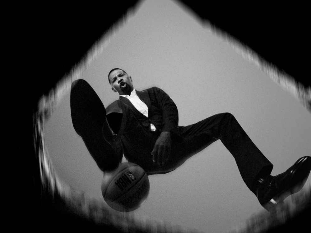 Black and white low angle photo of a man in a suit stepping on a basketball, creating a dynamic and surreal composition.