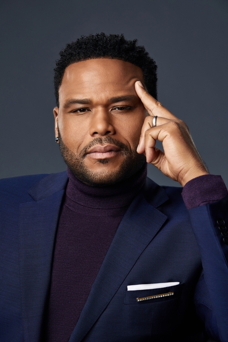 Portrait of a handsome adult Black man in a suit and turtleneck, thoughtfully posing against a dark gray background with direct studio lighting.