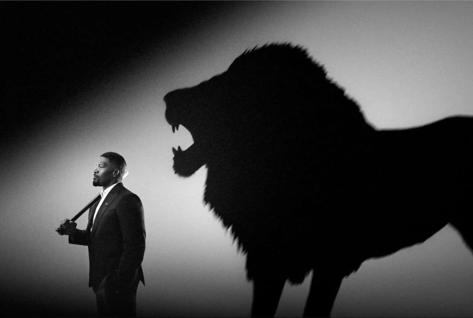 Monochrome portrait of a Black man in a suit with a lion shadow roaring behind him, showcasing ambition and inner strength.