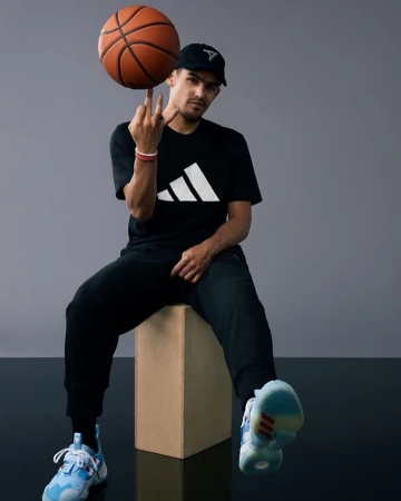 Young man sitting on a wooden box spinning a basketball on his finger against a grey studio background, photographed by Erik Umphery.