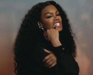 Close-up portrait of a Black woman with long curly dark hair wearing a black top and gold grillz, photographed by Erik Umphery