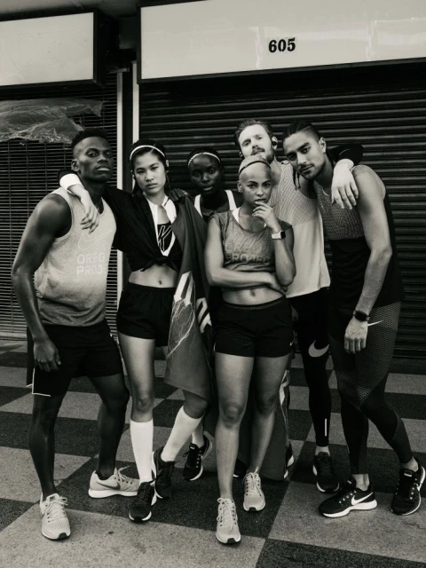 Group of six diverse athletes in athletic wear standing outdoors in front of a closed garage door with number 605 above.