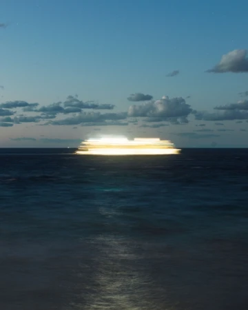 Long exposure of a boat at sea creating light trails, under a twilight sky with scattered clouds, ocean reflecting light.