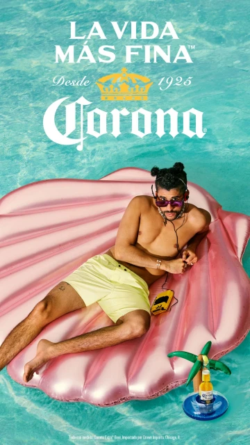 Man relaxes on seashell float in pool with Corona beverage; clear turquoise water, tropical vacation mood, leisure, and vibrant summer scene.