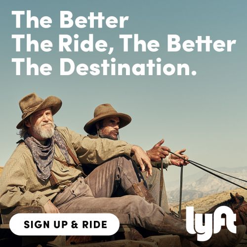 Two adult males in Western-style outfits ride in a horse-drawn carriage, set against a clear blue sky and desert backdrop. Lyft advertisement.