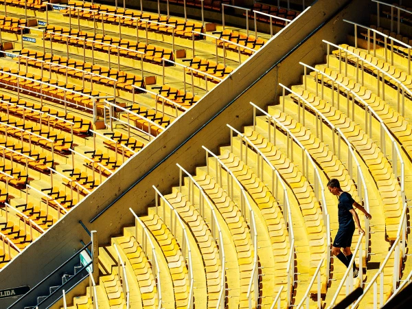 Stadium seating with a lone adult male walking down the stairs on a sunny day, bright yellow seats, and white railings.