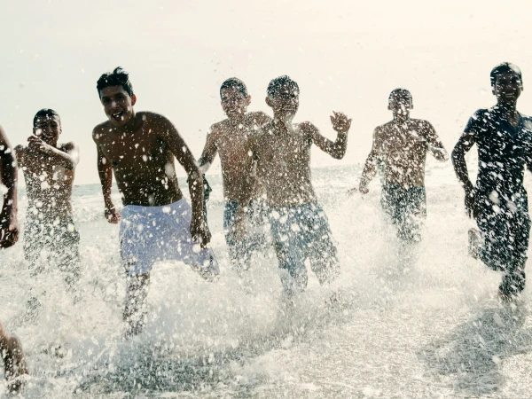 Group of boys running through ocean surf on a sunny day. Children are smiling as they splash in the water along the shoreline.