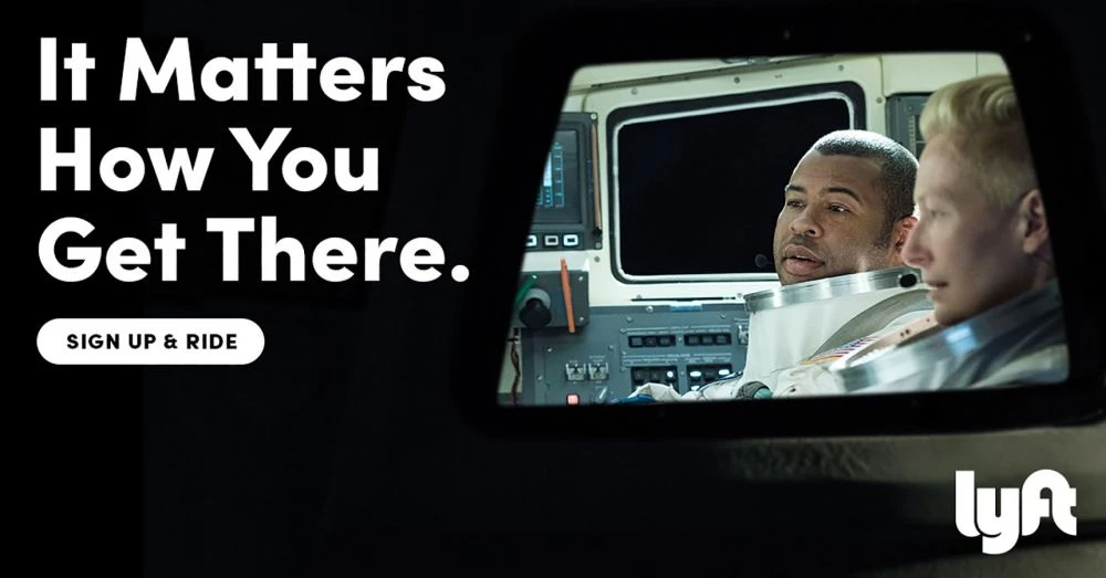 Two astronauts inside a space shuttle cockpit for a Lyft advertisement with text overlay promoting signing up and riding.