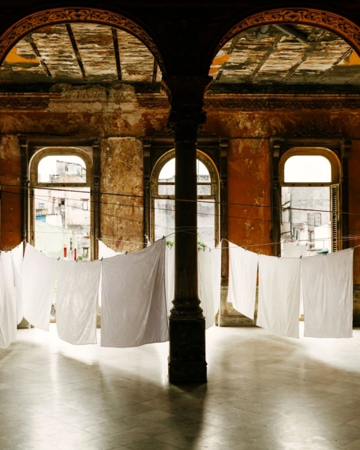 Indoor view of white sheets hanging to dry with orange walls and large windows in the background, creating a vintage atmosphere.
