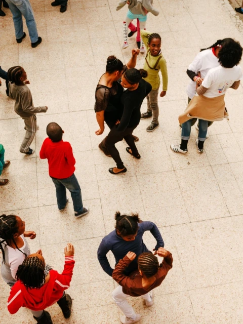 Overhead shot of large group of young people and adults dancing in an indoor space. They're in casual clothing with light neutral flooring.