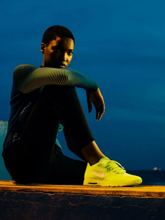 An athletic woman in sportswear is sitting in a neon-lit outdoor environment wearing vibrant neon yellow Nike sneakers.