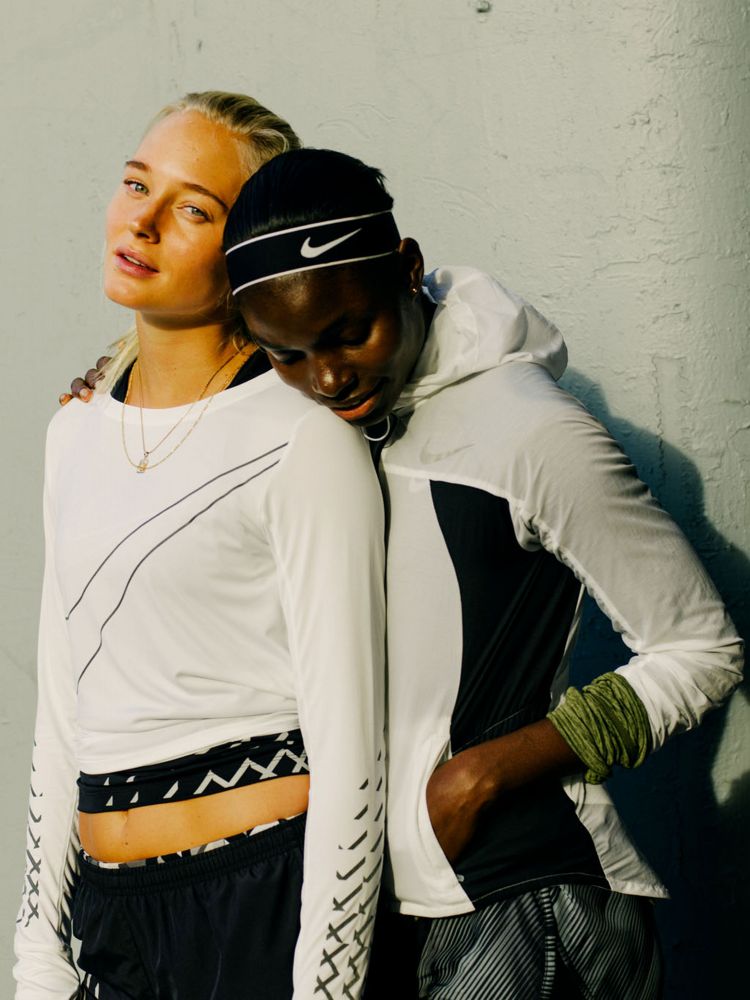 Two athletic women in Nike apparel stand together against a neutral wall, showcasing sportswear and fitness fashion.