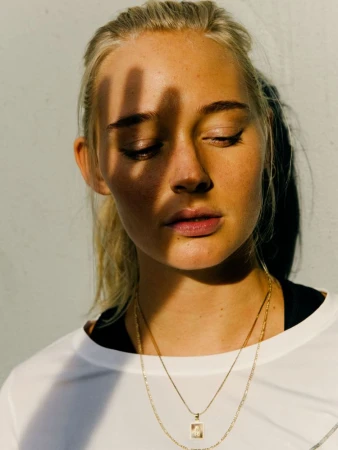 Close-up portrait of a woman with a hand shadow cast across her face wearing gold chain necklaces and a white t-shirt by João Canziani