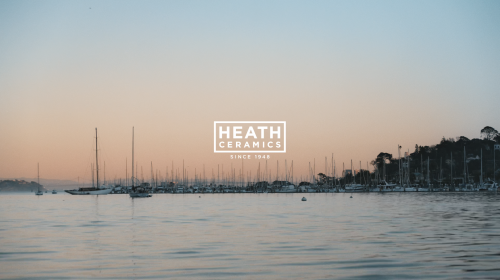 Scenic view of Heath Ceramics on the water with sailboats docked, capturing a serene, harbor scene at twilight.