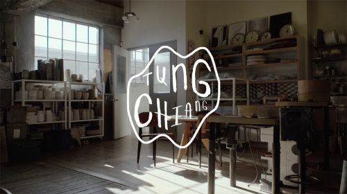 Indoor shot of a bright artist studio featuring shelving with ceramic wares, tables, chairs, and logo typography in the foreground.
