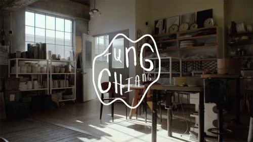 Indoor shot of a bright artist studio featuring shelving with ceramic wares, tables, chairs, and logo typography in the foreground.