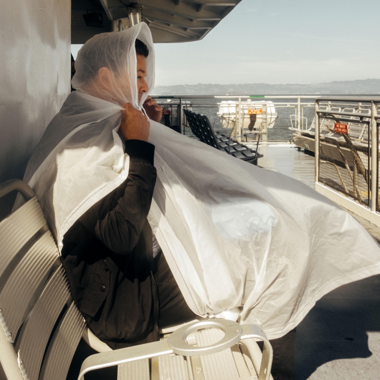 Person sitting on a boat under a semi-transparent cover, seascape background, outdoors on a clear day with bright, diffused lighting.